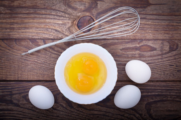 Raw eggs in bowl for whipping on wooden. Baking ingredients.