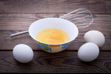 Raw eggs in bowl for whipping on wooden. Baking ingredients.