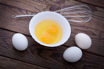 Raw eggs in bowl for whipping on wooden. Baking ingredients.