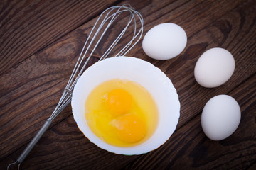 Raw eggs in bowl for whipping on wooden. Baking ingredients.