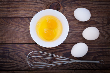 Raw eggs in bowl for whipping on wooden. Baking ingredients.