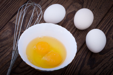 Raw eggs in bowl for whipping on wooden. Baking ingredients.