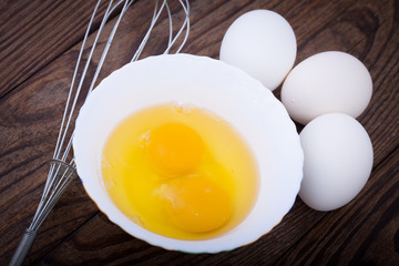 Raw eggs in bowl for whipping on wooden. Baking ingredients.