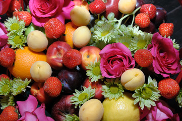 Früchte und Blumen. Hintergrund mit Früchten und Blumen. Die Obsternte. Die Textur der Frucht. Der blumige Hintergrund. Sortiertes Obst. Früchtekorb. Festliche Früchte gesetzt.