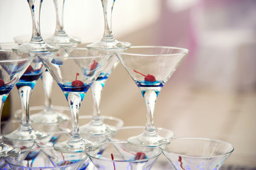 Glass goblets. Pyramid of champagne. The hill of glasses of wine and cherries. Glasses for alcohol. Festive drink. Bartender show. Decorations for the Banquet.