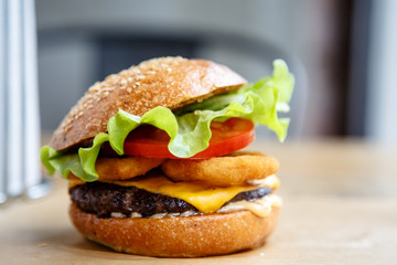 Burger with onion rings, lettuce and tomato lies on the table