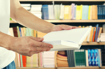Male hands holding open book on bookshelves background