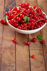 Fresh red currants in bowl on wooden table close up