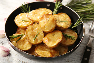 Delicious baked potato with rosemary in frying pan on table close up
