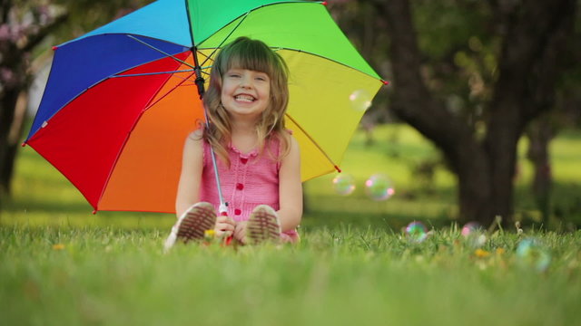 Girl with umbrella sitting on grass and smiling
