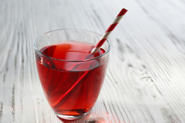 A glass of tasty garnet juice with a straw, on wooden background