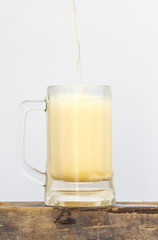International beer day with pouring beer into mug on wood and white background.