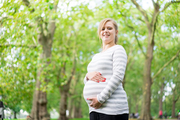 Naklejka na ściany i meble Happy and young pregnant woman in park in summer
