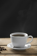 Cup of coffee and coffee grains on wooden table, on gray background