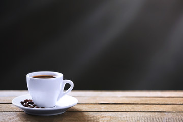 Cup of coffee and coffee grains on wooden table, on gray background