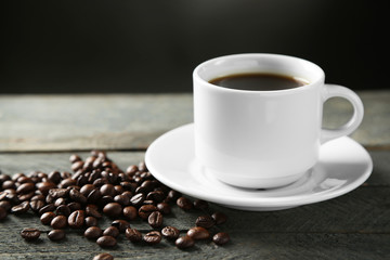 Cup of coffee and coffee grains on wooden table, on gray background