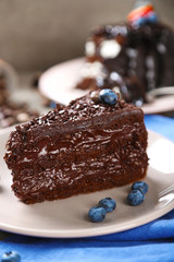Chocolate cake with chocolate cream and fresh blueberries on plate, on wooden background