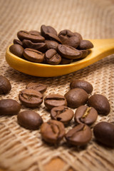 Heap of coffee beans with wooden spoon on jute canvas