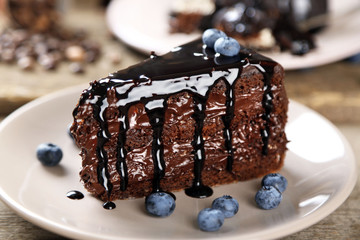 Chocolate cake with chocolate cream and fresh blueberries on plate, on wooden background