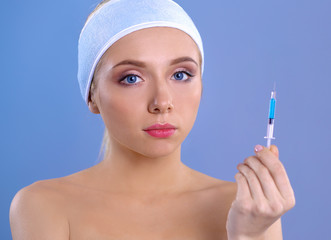 Young beautiful woman with syringe in her hand. Isolated on gray background
