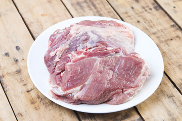 Raw pork on white dish, wooden table.