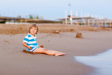 Happy little kid boy having fun with sand castle by ocean