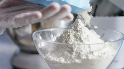 Hands pouring flour into a mixing bowl