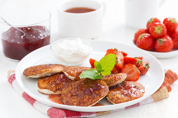 Pancakes with fresh strawberries on a plate, jam and tea.