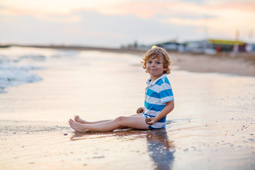 Fototapeta na wymiar Happy little kid boy having fun with sand castle by ocean