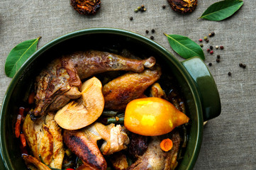 Top view of fried and baked chicken with vegetables in round ceramic stew pot on linen fabric background