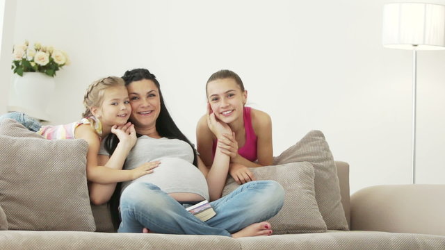 Pregnant girl kissing her daughters and smiling