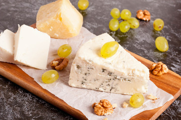 Blue cheese with grapes and nuts on wooden cutting board