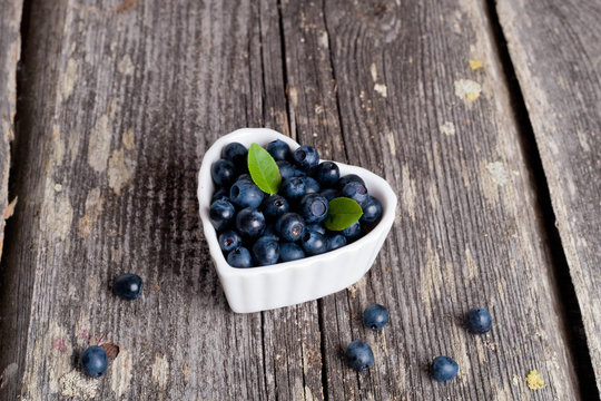 Heart shaped bowl of blueberries on wooden table