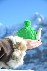 Tea pot in the knotted cap in the hand against alpine scenery