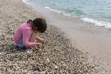 Little Girl collects stones on the seaside 