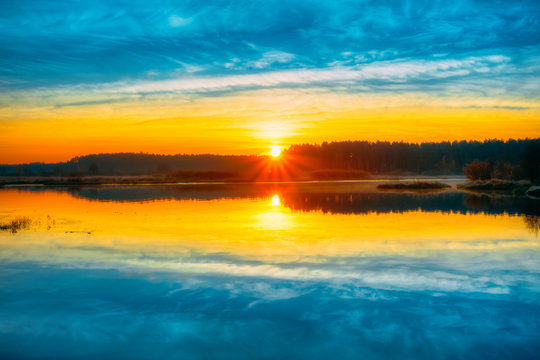 Bright beautiful Sunrise over Calm Lake, River and forest horizo