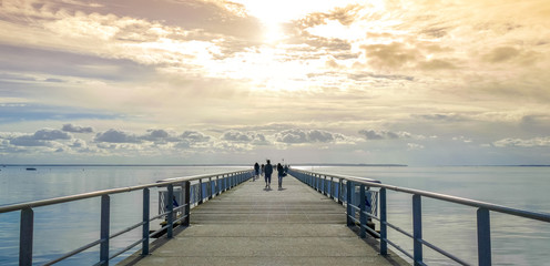 Long pier over the sea shore with sihouette of walkers