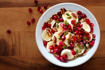 Bowl of healthy breakfast oatmeal with pomegranate, bananas, seeds and nuts, overhead view on wood
