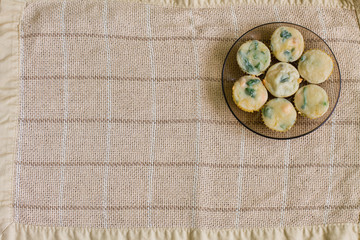 Seven muffins with salmon, spinach and cheese in small black glass plate on beige linen tablecloth. Aerial view.