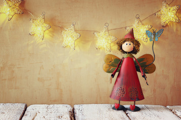 cute fairy on wooden table in front of stars garland with gold light background