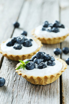 Dessert tartlets with blueberries on grey wooden background