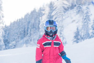 Little seven years old skier in red suit blue helmet and goggles