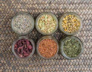 Dried herbal tea Japanese green tea, chamomile, linden flower, hibiscus, rooibos, lavender in mason jars over wooden background