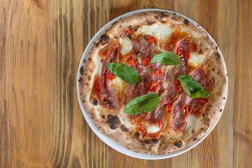 wood fired pizza with tomato, mozzarella chilly and fresh basil on wooden table