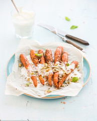 Roasted young carrots with cream and seeds in ceramic plate over blue wooden background