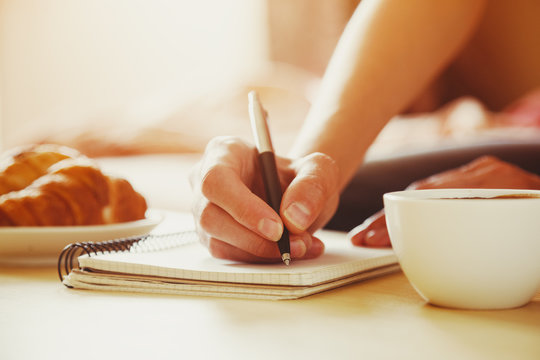female hands with pen writing on notebook with morning coffee an