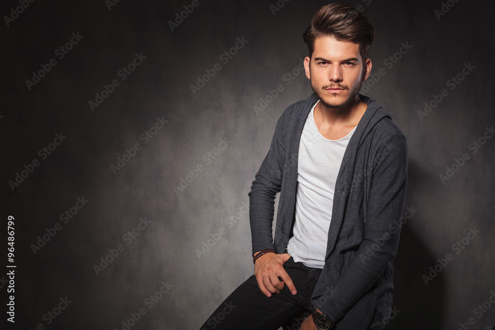 Wall mural man posing in studio with hand in pocket while sitting