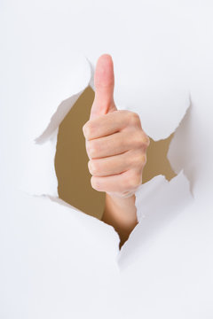 Hand through the hole in paper with woman thumb up