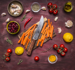 Healthy foods, cooking and vegetarian concept cutting board with a knife and sliced carrots around lie ingredients on wooden rustic background  top view
