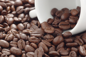 Heap of roasted coffee beans and white coffee cup lying on side